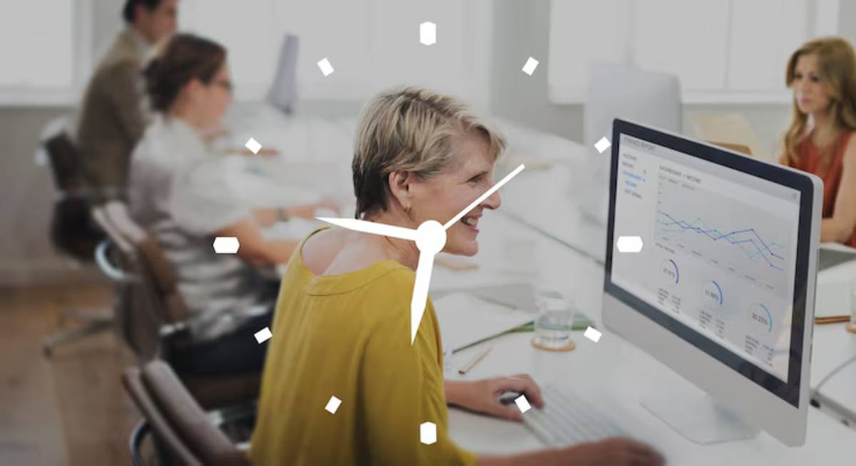 A woman sits at a desk working on a computer, with data charts displayed on the screen in a modern office environment.