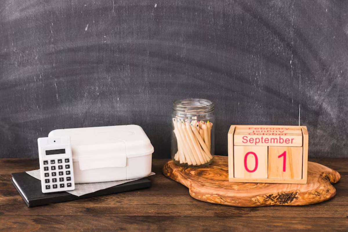 A calculator, a white box, a jar of colored pencils, and a wooden block calendar displaying September 01 on a rustic wooden surface.