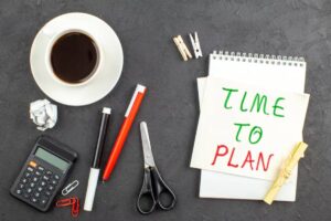 A workspace featuring a cup of coffee, stationery items, scissors, a calculator, and a notepad with "TIME TO PLAN" written on it.