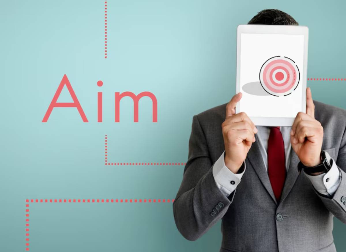 A businessman in a suit holds a tablet displaying a target graphic, with the word 