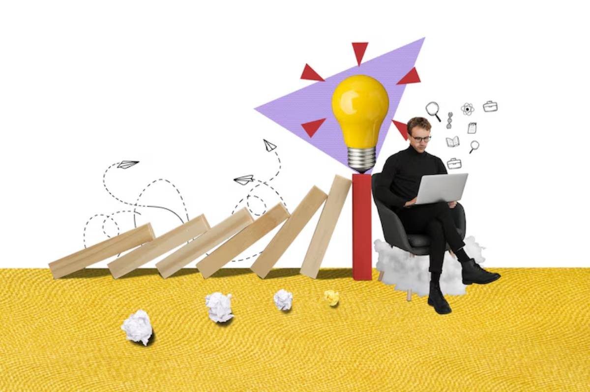 A person sits on a chair with a laptop, surrounded by wooden blocks, crumpled paper, and a large light bulb symbolizing ideas.