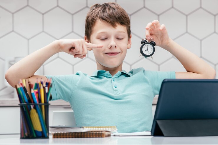 boy sitting in front of a tablet holding a alarm clock in hand